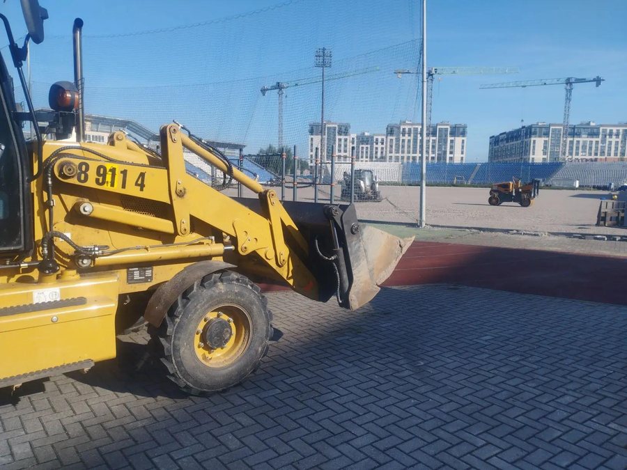 Экскаватор-погрузчик с поднятым передним ковшом на объекте в Калининграде